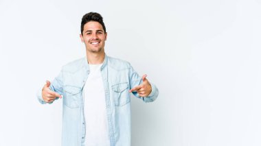 Beyaz arka planda yaşayan beyaz tenli genç bir adam gömlek fotokopi alanını gösteriyor, gururlu ve kendinden emin.