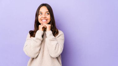 Genç, melez, yalnız bir kadın ellerini çenesinin altında tutuyor ve mutlu bir şekilde yan tarafa bakıyor..