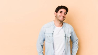 Bej arka planda izole edilmiş genç adam mutlu, güler yüzlü ve neşeli.