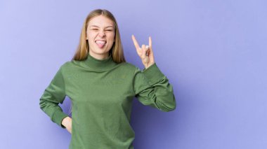 Mor arka planda izole edilmiş genç sarışın kadın parmaklarıyla taş hareketi gösteriyor.