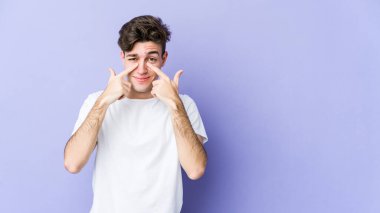 Mor arka planda izole edilmiş genç beyaz bir adam ağlıyor, bir şeyden memnun değil, acı ve kafa karışıklığı konsepti..