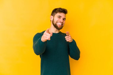 Sarı arka planda izole edilmiş genç beyaz adam parmaklarıyla ön tarafı işaret ediyor..
