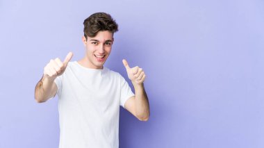 Young caucasian man isolated on purple background raising both thumbs up, smiling and confident. clipart
