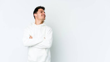 Beyaz arka planda izole edilmiş genç beyaz adam kollarını kavuşturarak gülümsüyor..