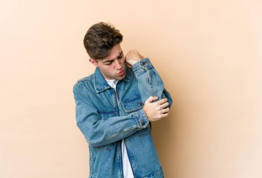 Beyazlı genç adam bej arka planda izole edilmiş dirsek masajı yapıyor, kötü bir hareketin ardından acı çekiyor..