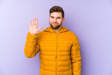 Mor arka planda izole edilmiş genç adam gülümseyerek beş numarayı parmaklarıyla gösteriyor..