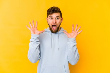 Sarı arka planda izole edilmiş genç beyaz adam gökyüzüne haykırıyor, yukarı bakıyor, hayal kırıklığına uğramış..