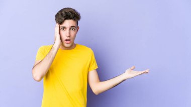 Mor arka planda izole edilmiş genç beyaz adam, avuç içi fotokopi alanını elinde tutmaktan etkilenmiş..