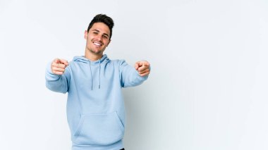 Beyaz arka planda izole edilmiş genç beyaz adam parmaklarıyla ön tarafı işaret ediyor..