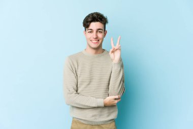 Mavi arka planda izole edilmiş genç beyaz adam iki numarayı parmaklarıyla gösteriyor..