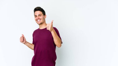 Beyaz arka planda izole edilmiş genç beyaz bir adam iki parmağını da kaldırıyor, gülümsüyor ve kendinden emin..