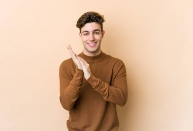 Beyaz tenli genç adam bej arka planda izole edilmiş enerjik ve rahat hissediyor, ellerini ovuşturuyor kendinden emin..