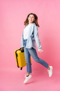 Genç beyaz kadın pembe arka planda izole edilmiş bir şekilde gezginlere gidiyor.