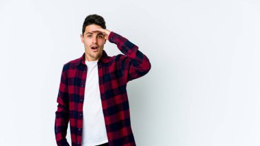 Beyaz arka planda izole edilmiş genç beyaz bir adam uzaklara bakıyor ve elini alnına koyuyor..