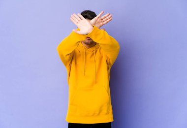 Mor arka planda izole genç beyaz adam iki kolu çapraz tutuyor, inkar kavramı.