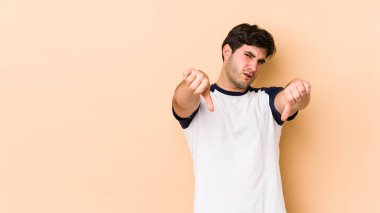 Bej arka planda izole edilmiş genç bir adam baş parmağını aşağı gösteriyor ve hoşlanmadığını ifade ediyor..