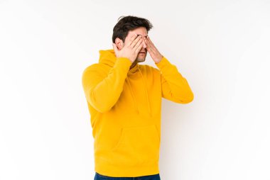 Beyaz arka planda izole edilmiş genç adam elleriyle gözlerini kapatmaktan korkuyor..