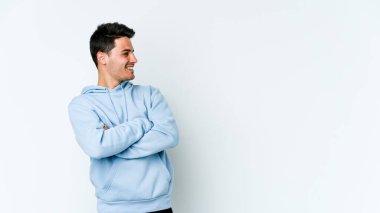 Beyaz arka planda izole edilmiş genç beyaz adam kollarını kavuşturarak gülümsüyor..