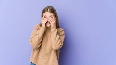 Mor arka planda izole edilmiş genç sarışın kadın kameraya parmaklarıyla göz kırpıyor, yüzünü kapatmaktan utanıyor..