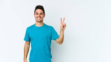 Beyaz arka planda izole edilmiş genç beyaz bir adam neşeli ve kaygısız parmakları olan bir barış sembolü gösteriyor..