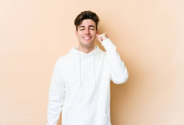 Beyazlı genç adam bej arka planda izole edilmiş zafer, tutku ve coşkuyu kutluyor, mutlu bir ifade..