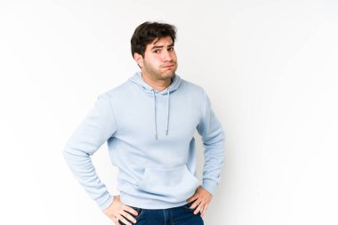 Beyaz arka planda izole edilmiş genç adam kafası karışmış, şüpheli ve güvensiz hissediyor..
