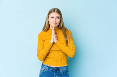 Genç sarışın kadın mavi arka planda izole edilmiş dua ediyor, bağlılık gösteriyor, dindar biri ilahi ilham arıyor..