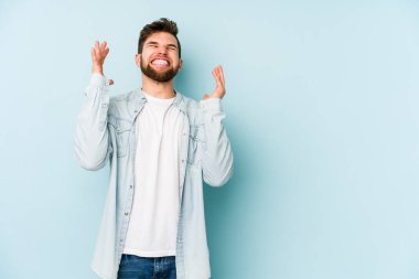 Kafkasyalı genç adam mavi arka planda izole edilmiş neşeli bir şekilde gülüyor. Mutluluk kavramı.