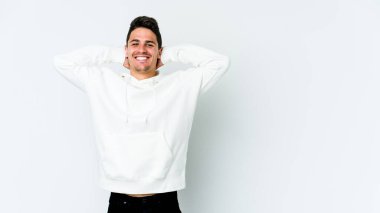 Beyaz arka planda izole olmuş genç beyaz bir adam kendini güvende hissediyor, elleri başının arkasında..