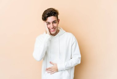 Beyazların arka planında izole edilmiş genç beyaz adam mutlu bir şekilde gülüyor ve ellerini karnının üstünde tutarak eğleniyor..