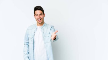 Beyaz arka planda izole edilmiş genç beyaz bir adam selamlama jesti olarak kameraya elini uzatıyor..