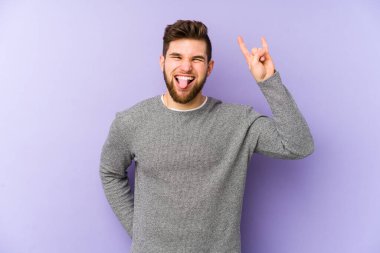 Mor arka planda izole edilmiş genç beyaz adam parmaklarıyla taş hareketi gösteriyor.