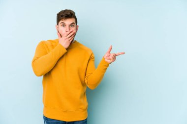 Mavi arka planda izole edilmiş genç beyaz adam yan tarafı işaret ediyor.