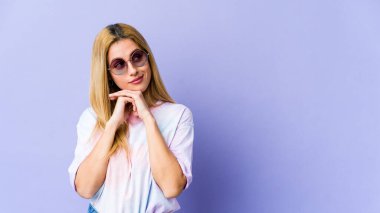 Sarışın, beyaz bir kadın ellerini çenesinin altında tutuyor ve mutlu bir şekilde yan tarafa bakıyor..