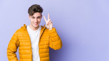 Mor arka planda izole edilmiş genç beyaz adam iki numarayı parmaklarıyla gösteriyor..