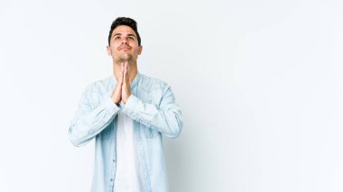 Beyaz arka planda izole edilmiş genç beyaz bir adam el ele tutuşup, ağız kenarında dua ediyor, kendinden emin..