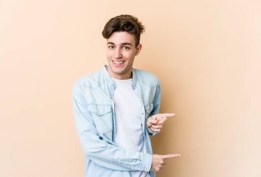 Beyazlı genç adam bej arka planda izole edilmiş. İşaret parmaklarıyla işaret ettiği için heyecanlı..