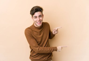 Beyaz tenli genç adam bej arka planda izole edilmiş ve işaret parmağıyla fotokopi alanını işaret ederek heyecan ve arzusunu ifade ediyor..