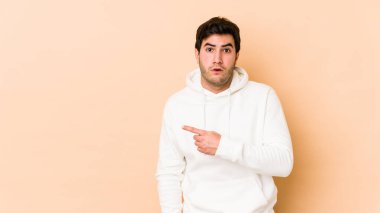 Bej arka planda izole edilmiş genç adam yan tarafı işaret ediyor.