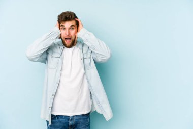 Genç beyaz adam mavi arka planda izole edilmiş bağırıyor, çok heyecanlı, tutkulu, bir şeyden memnun..