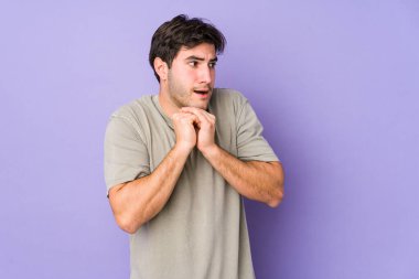 Mor arka planda izole edilmiş genç bir adam şans için dua ediyor, şaşırmış ve ağzı açık bir şekilde önüne bakıyor..