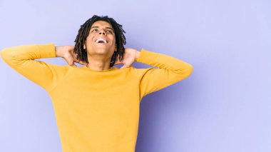 Rasta saç stili giyen genç siyahi adam kendinden emin ve elleri başının arkasında..