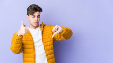 Mor arka planda izole edilmiş genç beyaz adam baş parmağını kaldırıyor ve baş parmağını aşağı gösteriyor, zor seçim kavramı.