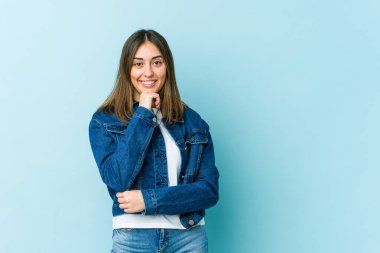 Genç beyaz kadın mutlu ve kendinden emin gülümsüyor, elleriyle çenesine dokunuyor..