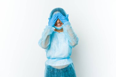 Beyaz arka planda soyutlanmış genç bir cerrah. Elleriyle gözlerini kapatıyor. Gülümsüyor ve bir sürpriz bekliyor..