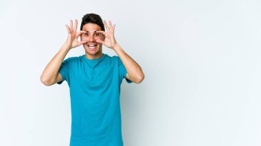 Beyaz arka planda izole edilmiş genç beyaz bir adam bir başarı fırsatı bulmak için gözlerini açık tutuyor..