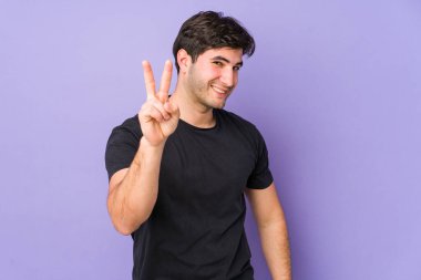 Mor arka planda izole edilmiş genç bir adam iki numarayı parmaklarıyla gösteriyor..