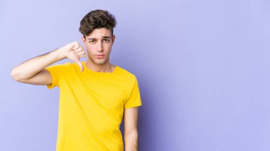 Mor arka planda izole edilmiş genç beyaz bir adam hoş olmayan bir jest yapıyor, başparmakları aşağıda. Anlaşmazlık konsepti.