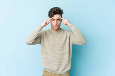 Kafkasyalı genç adam mavi arka planda izole edilmiş bir göreve odaklanmış, parmaklarını işaret ediyor..