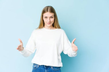 Mavi arka planda izole edilmiş genç sarışın kadın iki eliyle bir şey tutuyor, ürün sunumu..